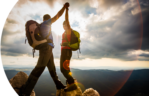 Hikers holding hands looking at a sunset.