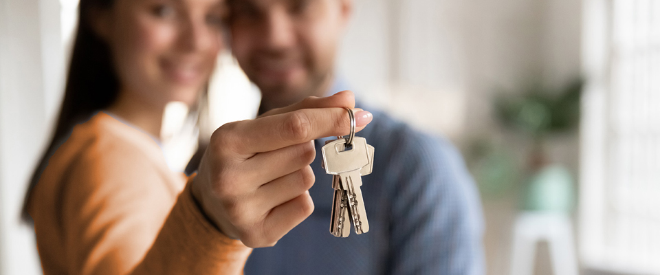 A man and woman holding up keys to their new house