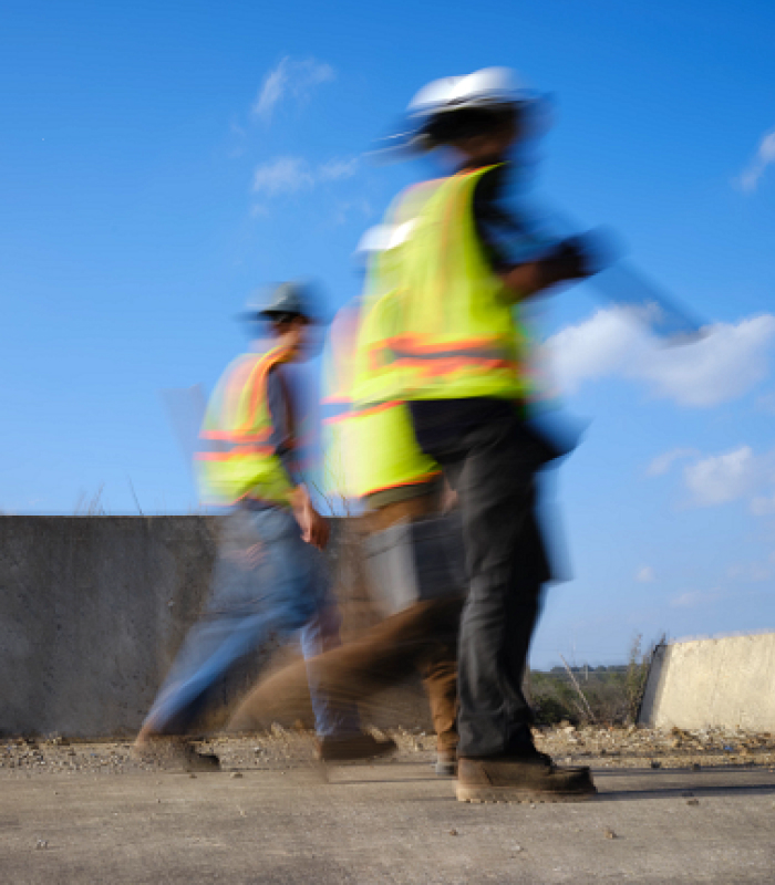 3 men walking on a job site with bright vests on, blurry to indicate action