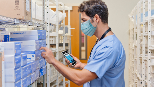 Nurse referencing a Zebra mobile computer while looking for supplies in the stockroom