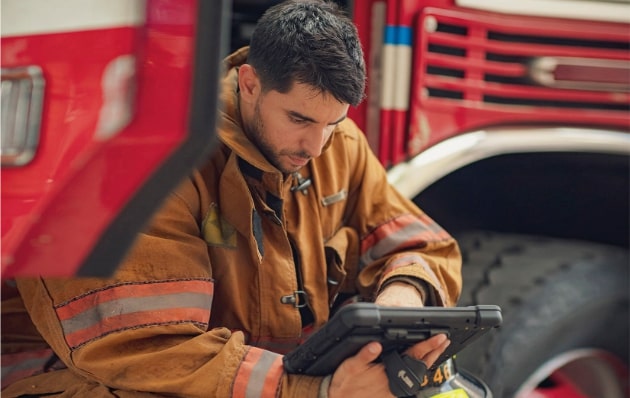 Fireman sitting down on steps of fire truck checking something out on his Zebra tablet