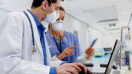 Doctor typing on a laptop while a nurse shares information from a Zebra mobile computer