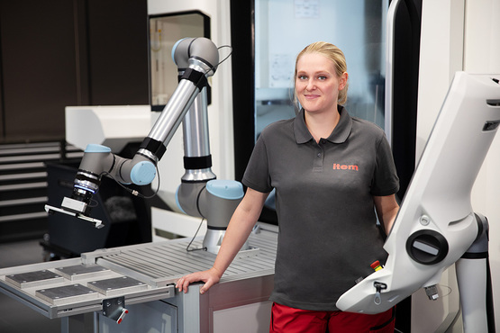 item Mitarbeiterin steht neben einer mobilen Roboter-Basis, auf der ein Cobot montiert ist.